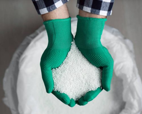 Renewable UREA Farmer holding pile of ammonium nitrate pellets over bag, top view. Mineral fertilizer
